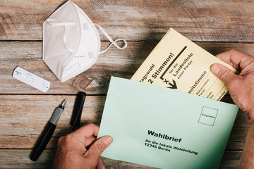 Hand putting ballot for federal elections into envelope on table with protective mask and corona rapid test