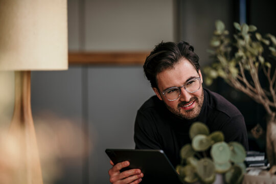 Smiling male professional looking away while holding digital tablet at home