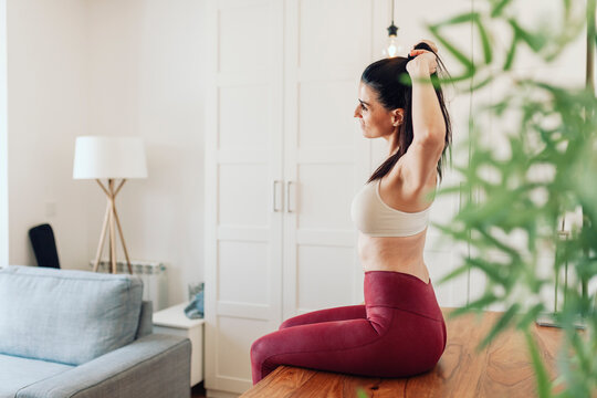 Mature woman tying ponytail while sitting on table in living room