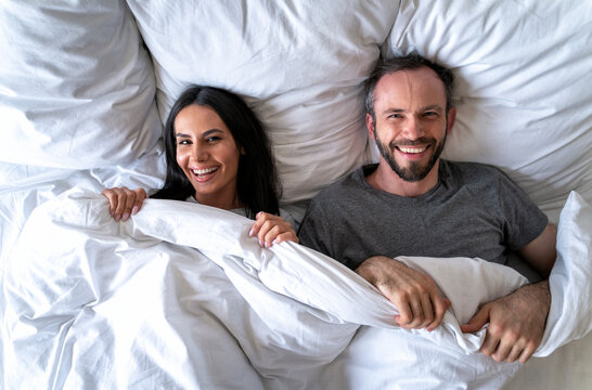 Happy couple with blanket lying on bed at home