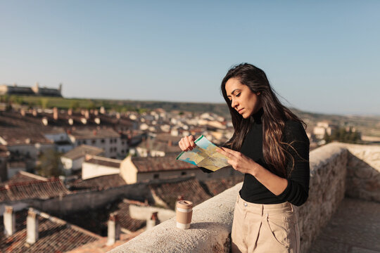 Female tourist checking map while standing by retaining wall