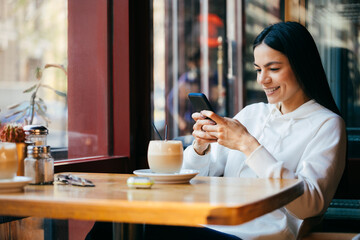 Smiling woman using mobile phone at cafe