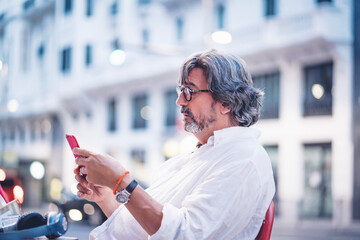Attractive senior man using smart phone while sitting at sidewalk cafe in Madrid