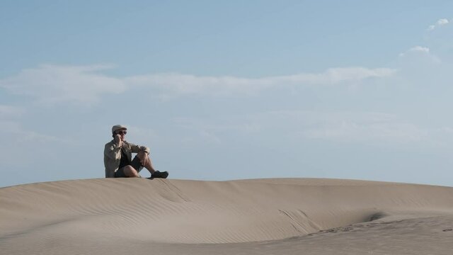 a young explorer seated on a hill in a desert and using an smartphone