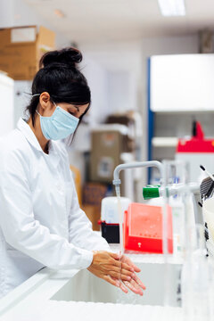Mature female researcher wearing protective face mask washing hands in laboratory