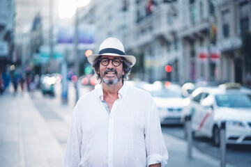 Portrait of attractive senior man with white clothing and hat posing at camera in street of Madrid