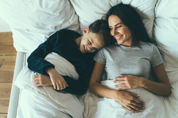 Smiling son and mother lying on bed at home