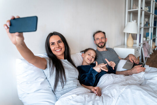 Woman taking selfie with family through smart phone on bed at home