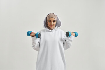 Beautiful young arabian girl in hijab lifting dumbbells