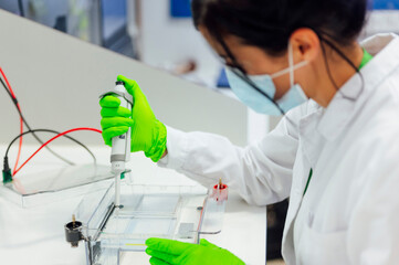 Female medical expert using pipette on electrophoresis apparatus while testing in lab