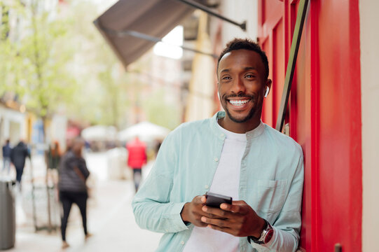 Smiling man with smart phone leaning on red wall