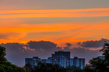 Bright orange blue sky at sunset over city buildings, orange trails leaved by airplanes