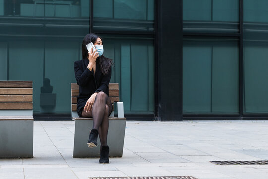 Woman with face mask talking on mobile phone while sitting on bench