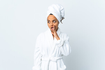 Young woman in bathrobe over isolated white background whispering something with surprise gesture while looking to the side
