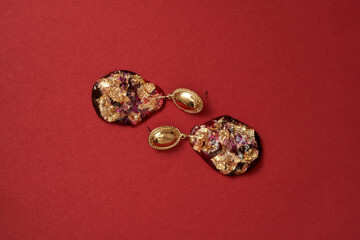 Flat lay of luxury gold earrings with precious stones lying horizontally isolated over red background