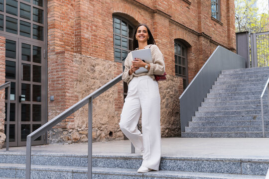 Smiling woman with laptop moving down from steps