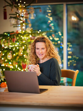 Smiling woman having coffee while looking at laptop during Christmas
