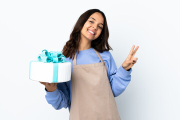 Pastry chef holding a big cake over isolated white background showing victory sign with both hands