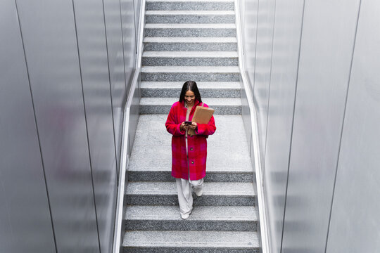 Young Woman Using Smart Phone While Walking On Steps