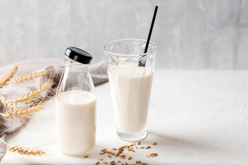Gluten free oat milk in a glass bottle and glass on a light background. Organic natural vegetarian drink without gluten and lactose. Health concept. Copy space.