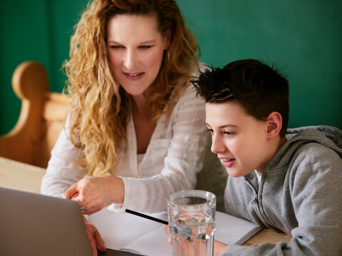 Mother pointing at laptop while teaching son in kitchen