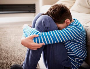 Sad boy hugging knees at sofa in living room