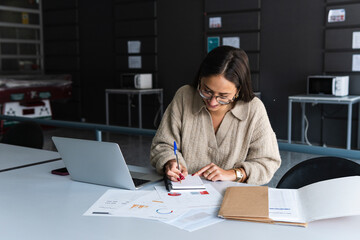 Female professional wearing eyeglasses writing on diary at office