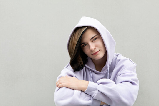 Beautiful girl in purple hooded shirt by gray wall