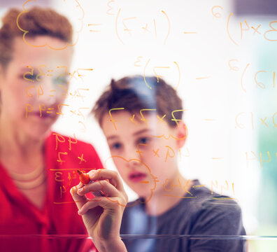 Boy writing on glass by mother while learning mathematics at home