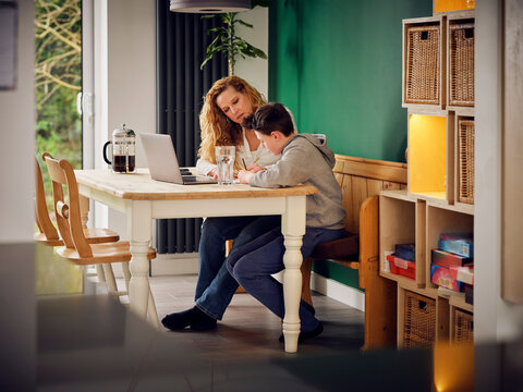 Mother teaching son at home in front of laptop at home