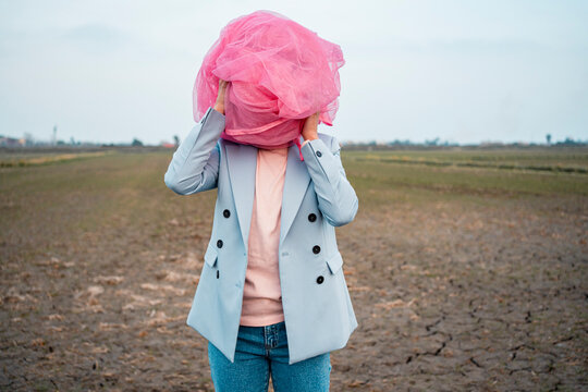 Woman in casuals covering face with pink tulle net on dirt field