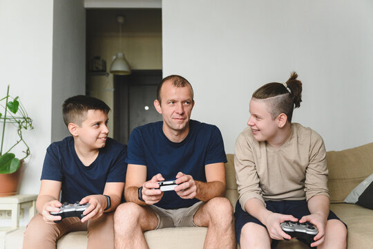 Father playing game with sons sitting on sofa at home
