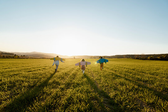 Brothers and sister with rocket wings running on agricultural field during sunny day