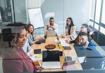 Female professional explaining business plan to colleagues during meeting seen through glass in coworking office