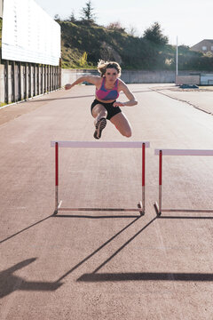 Young female athlete jumping over hurdle during sunny day
