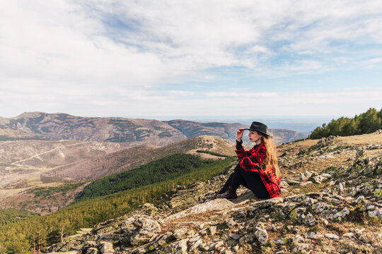 Young woman wearing hat contemplating while sitting on mountain during vacations