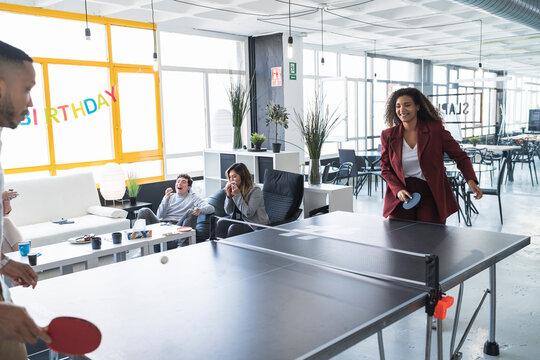 Smiling businesswoman playing ping pong with male colleague at coworking office