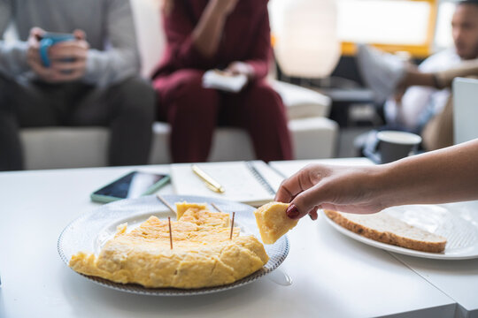 Businesswoman having Spanish omelet at table with colleagues in background