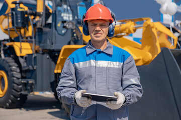 Senior excavator driver receives online order on tablet for work plan at factory site