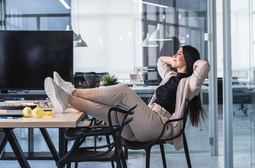 Businesswoman with hands behind head relaxing at hot desk in office