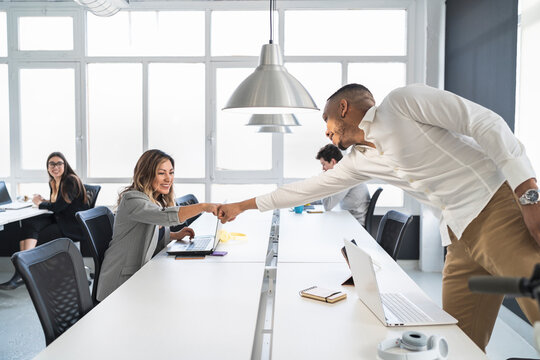 Smiling male and female entrepreneurs doing fists bump at desk in coworking office
