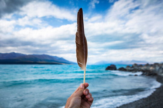 New Zealand, Canterbury, Hand holding feather with Lake Tekapo in background