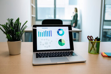 Chart on laptop screen while businesswoman standing near window at office