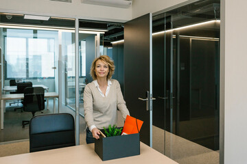 Female professional with box standing at desk in office