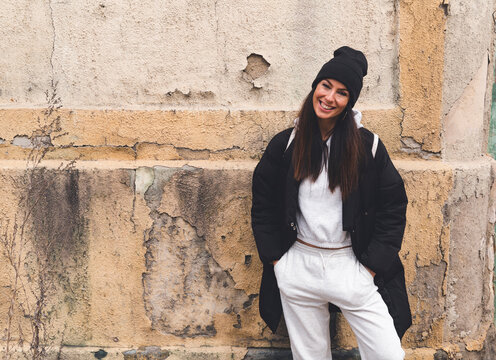 Smiling Woman Standing With Hands In Pockets In Front Of Wall