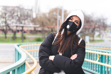 Woman wearing face mask and hooded jacket staring while standing with arms crossed
