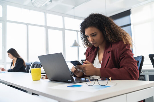 Businesswoman using mobile phone with female colleague working in background at coworking office