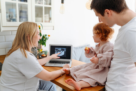 Smiling pregnant woman showing ultrasound image to daughter by father on table in living room
