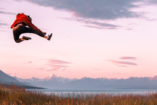 New Zealand, Canterbury, Rear view of young man jumping over Lake Pukaki at sunset