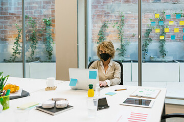 Businesswoman wearing protective face mask working on laptop at desk